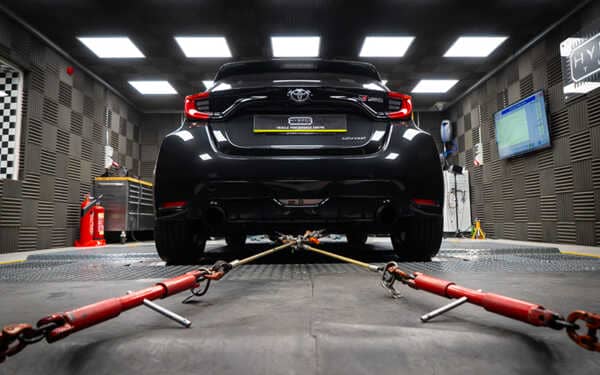 Dynamic lowdown shot of the back of a black Toyota GR Yaris chained down in Hybrid Tune dyno cell