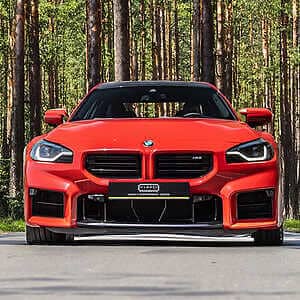 BMW G87 M2 tuning to achieve a potent output of 605+ BHP. Front view of a bright red BMW M2 parked on a road in a pine forest
