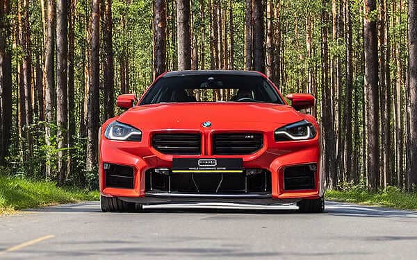 BMW G87 M2 tuning to achieve a potent output of 605+ BHP. Front view of a bright red BMW M2 parked on a road in a pine forest