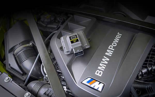 Our new Strat-2 BMW tuning device for the S58 engine. A picture of the device resting on top of the engine with BMW M power written on it