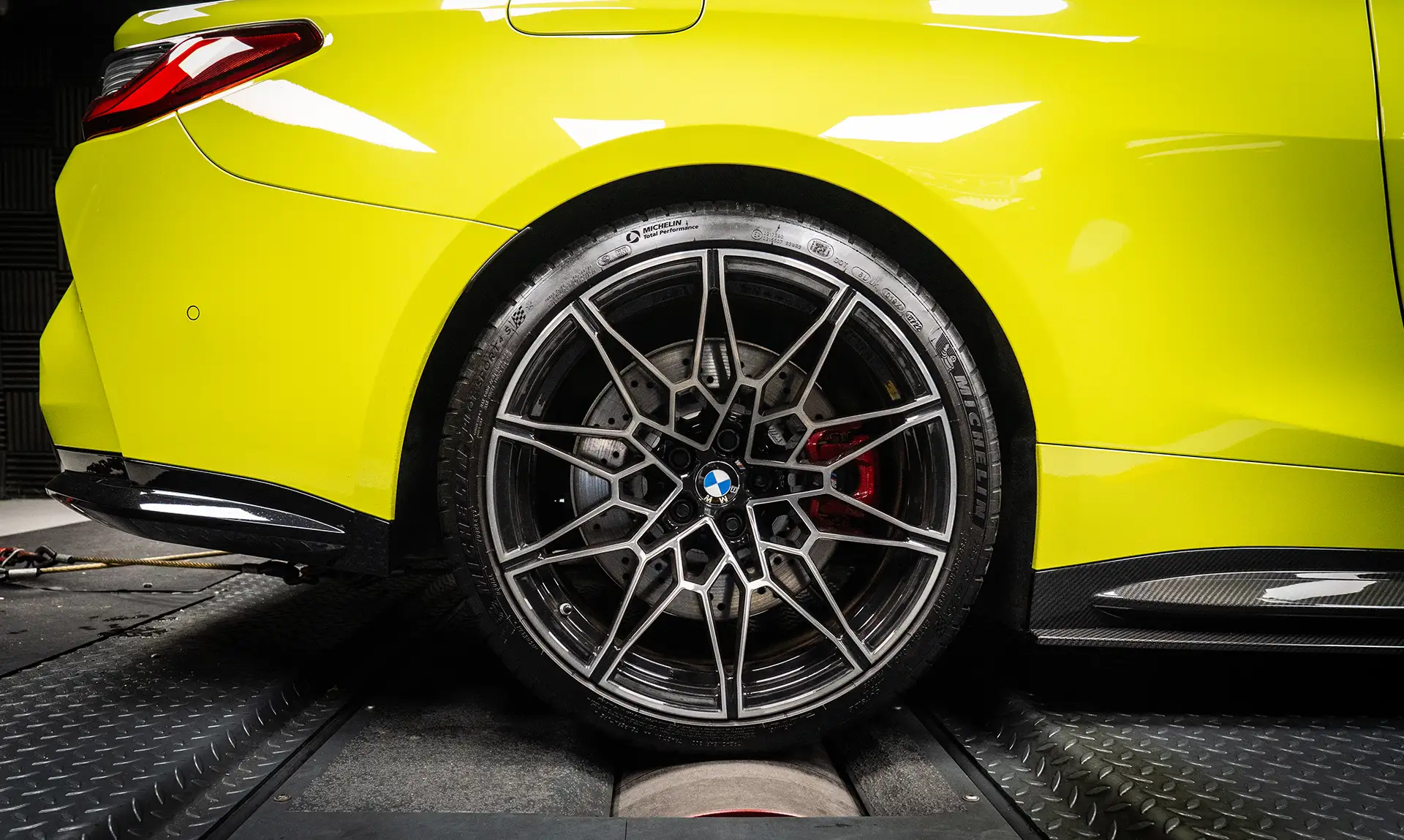 At Hybrid Tune you’re never going to see us advertising and selling a product without guaranteed backed dyno results, road testing and circuit testing. Yellow BMW G82 M4 having development work done on the dyno with our new tuning box. It is a close up shot of the tear wheel on a roller. The car is bright yellow, and the wheel is spoked silver with a red brake caliper. The background id dark grey
