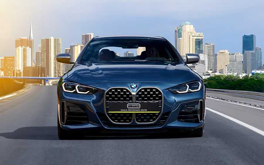 BMW M440i G22 Tuning Box B58TU Strat-2 1 BMW M440i G22 Tuning Box 450BHP 600NM front photo of a dark blue BMW with black grill parked on a grey road with blue sky and tower blocks in the backgtound